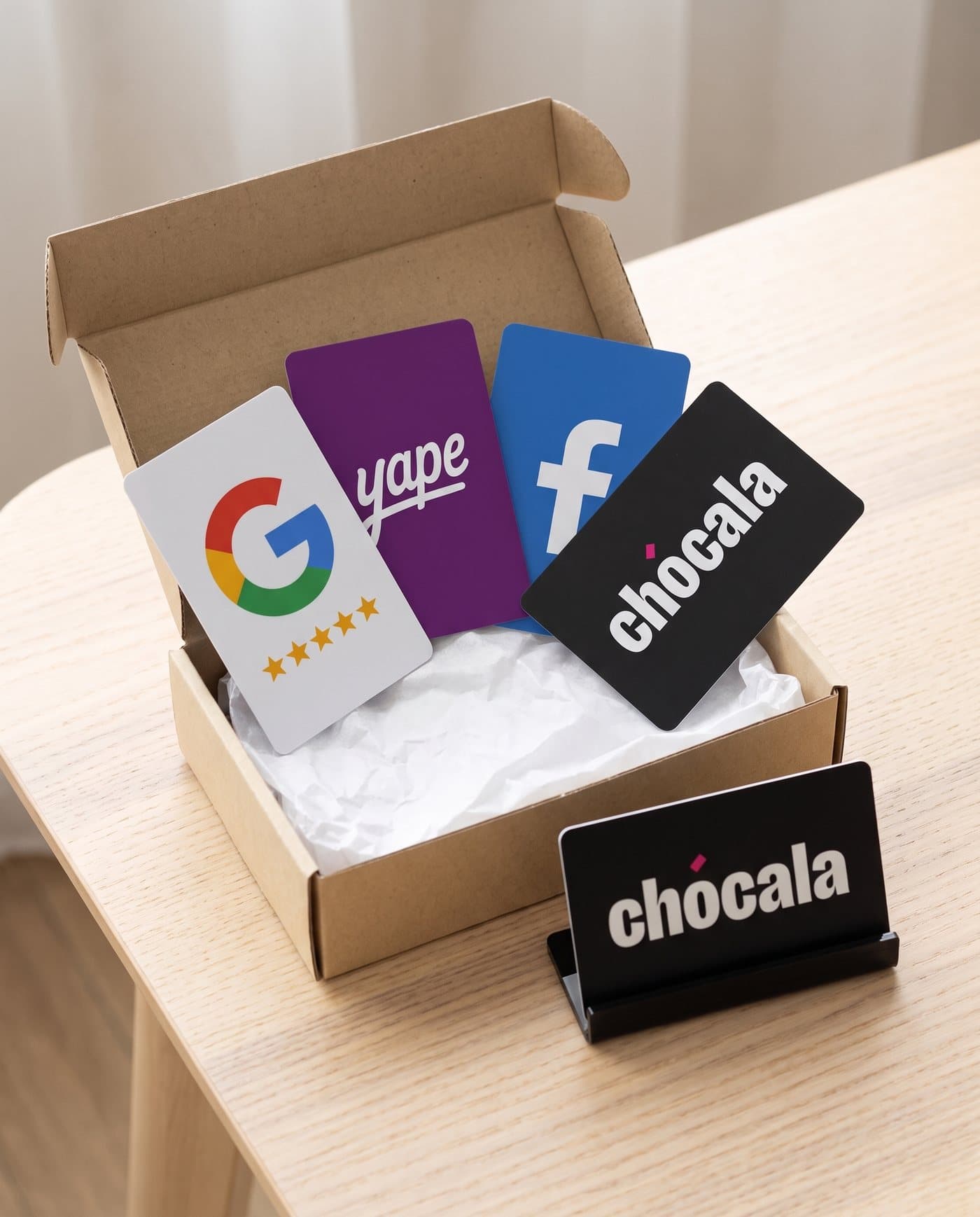 Caja de Chócala con cuatro tarjetas: Google, Yape, Facebook y Chócala, y el soporte de acrílico