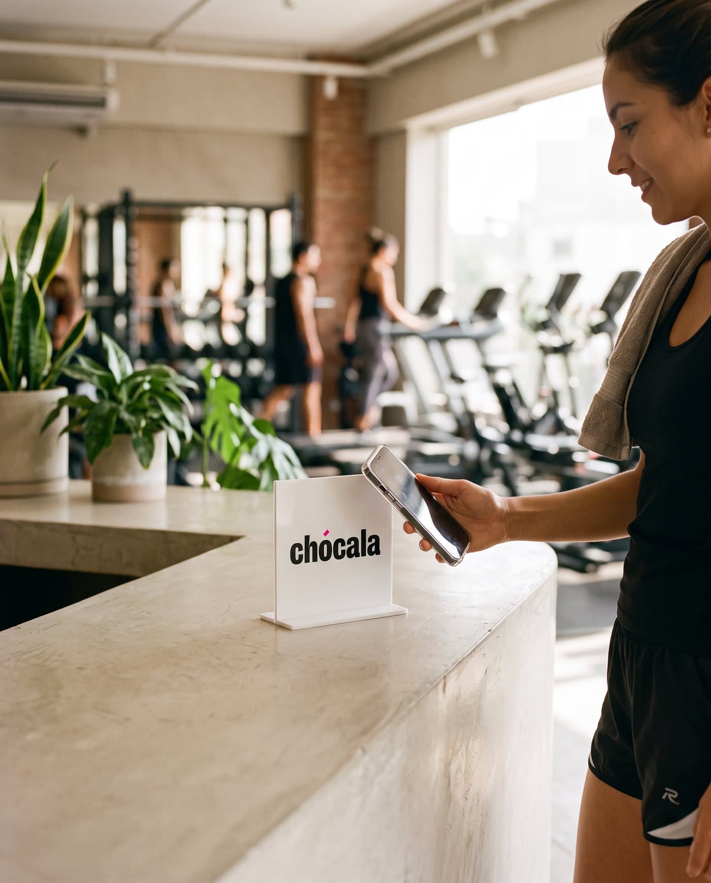 Mujer acercando su celular al soporte de Chócala en la recepción de un gimnasio